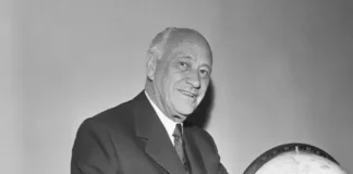 Conrad Nicholson Hilton smiling beside a globe, symbolizing his vision as the hotel magnate who built a worldwide hospitality empire