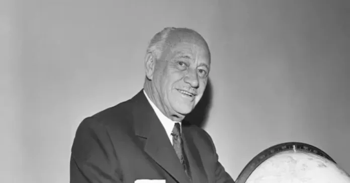 Conrad Nicholson Hilton smiling beside a globe, symbolizing his vision as the hotel magnate who built a worldwide hospitality empire