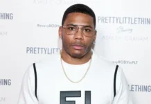 Nelly at a PrettyLittleThing event, wearing a white shirt and gold chain, representing his success and Nelly Net Worth.