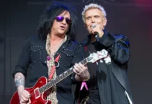 Steve Stevens performing live with Billy Idol holding red guitar on stage during concert showcasing his $45 million net worth career