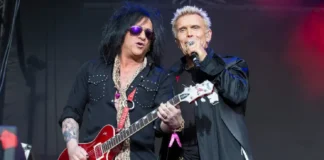 Steve Stevens performing live with Billy Idol holding red guitar on stage during concert showcasing his $45 million net worth career